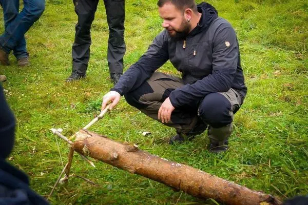 Mann zeigt auf eine Holzstruktur mit einem Stock auf dem Boden