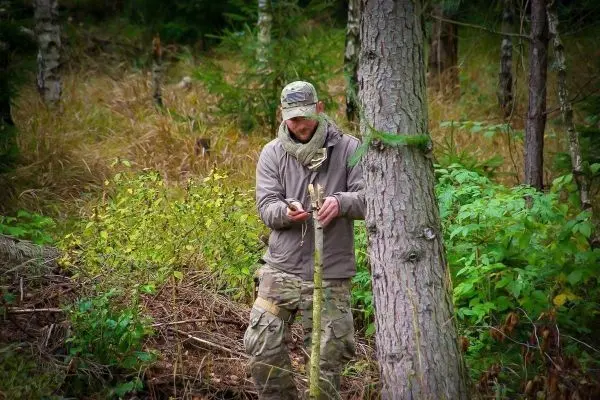 Messer bearbeitet einen Stock im Wald zwischen Bäumen und Sträuchern