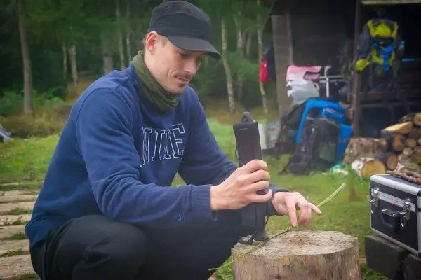 Person bearbeitet einen Stock auf einem Baumstumpf beim Survival Training