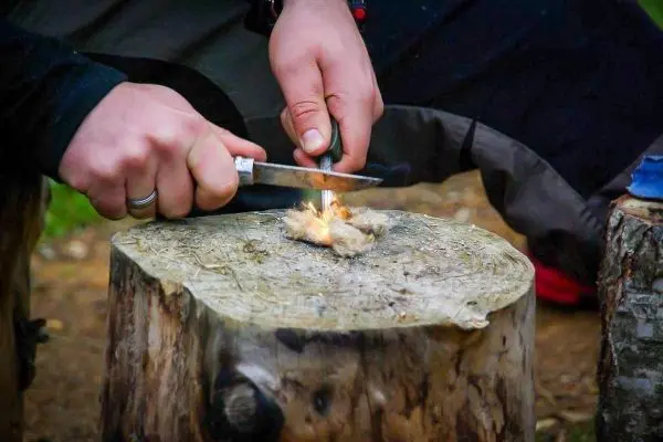 Person entzündet Feuer mit einem Messer auf einem Baumstumpf beim Survival Training