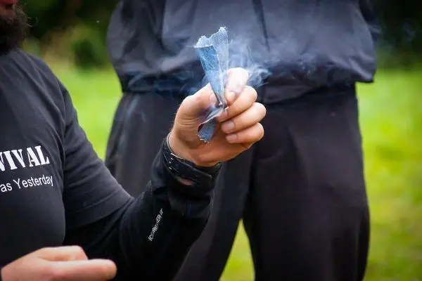 Person hält rauchendes Material in der Hand beim Survival Training