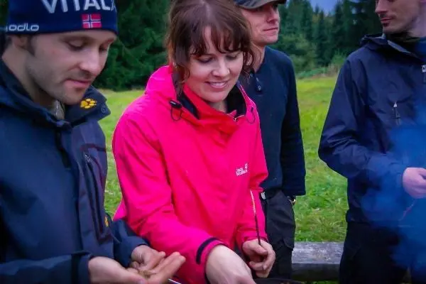 Person in pinker Jacke bereitet Essen am Feuer vor