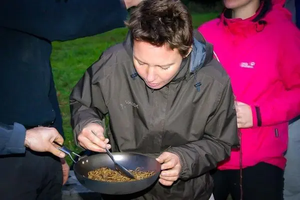 Person mit Schüssel isst mit Gabel, umgeben von anderen Personen