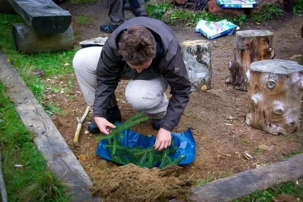 Person sammelt Zweige in einer blauen Plane
