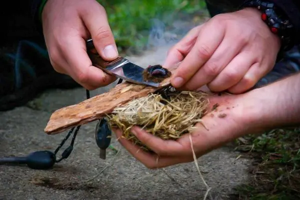 Person schneidet mit Messer Zunder auf Holzstück