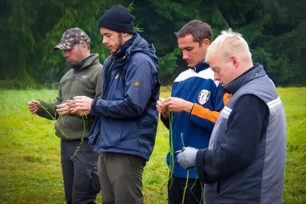Personen binden Pflanzenmaterialien zusammen beim Überlebenstraining