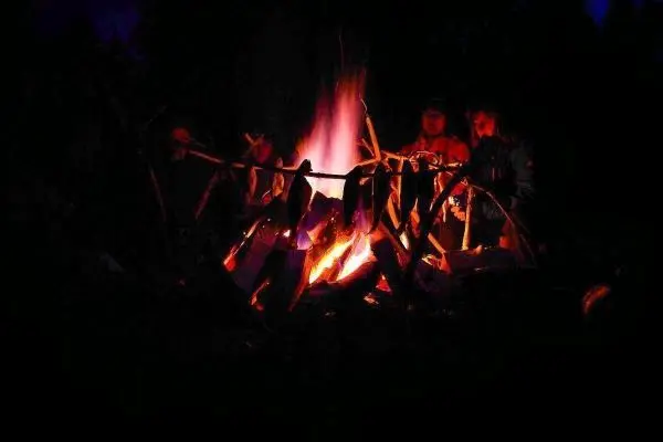 Personen sitzen um ein Feuer und halten Stöcke mit Essen