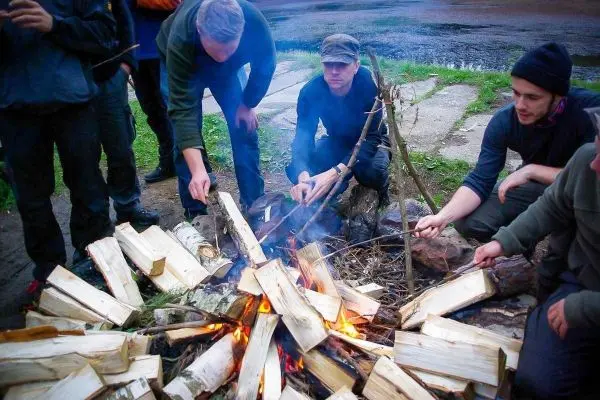Personen sitzen um ein Feuer und rösten Holzstücke beim Survival Training