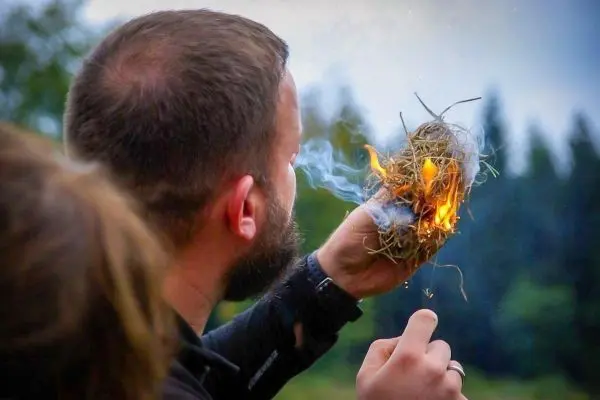 Zunder glimmt und raucht in der Hand, kleine Flamme sichtbar