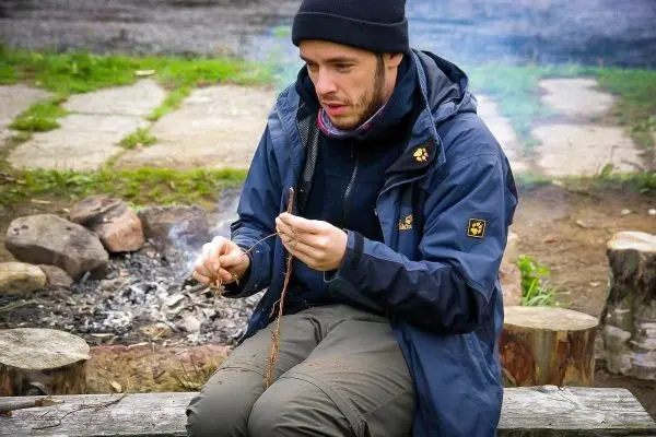 Zunder wird mit einem Stock bearbeitet, während Rauch vom Feuer aufsteigt