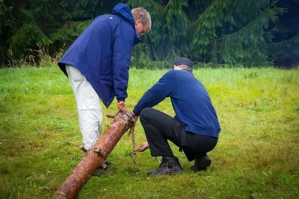 Zwei Personen arbeiten gemeinsam an einem Holzstück im Gras