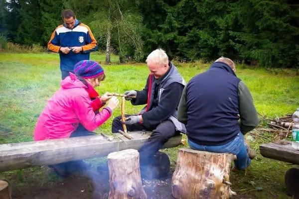 Zwei Personen bearbeiten Holzstücke auf einer Bank, während eine dritte Person im Hintergrund steht