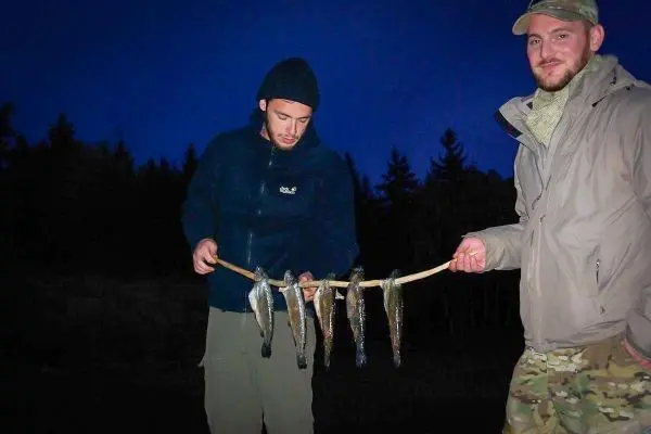 Zwei Personen halten einen Stock mit mehreren gefangenen Fischen