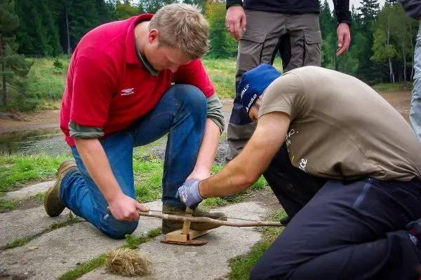 Zwei Personen nutzen eine Feuerbohrtechnik mit Holzstücken und Zunder