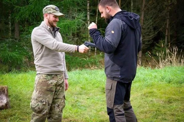 Zwei Personen üben den Umgang mit einer Handfeuerwaffe im Freien