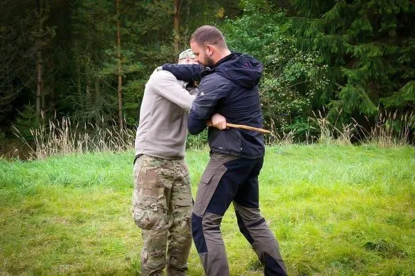 Zwei Personen üben eine Nahkampftechnik im Freien mit einem Stock