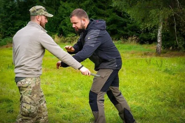 Zwei Personen üben eine Selbstverteidigungstechnik auf einer Wiese