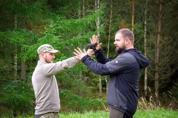 Zwei Personen üben eine Selbstverteidigungstechnik im Wald mit einer Handwaffe
