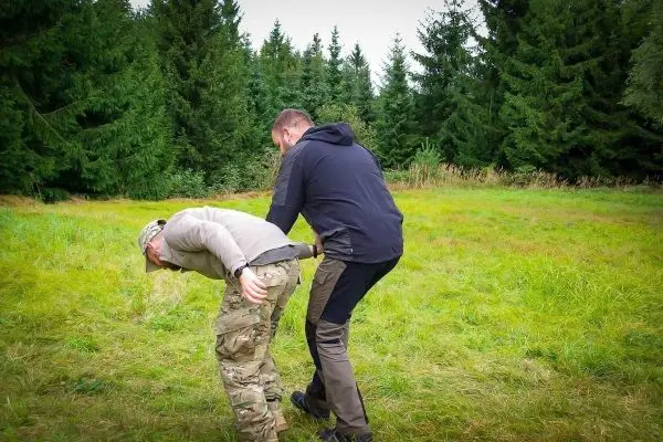 Zwei Personen üben eine Technik zur Kontrolle in einer Wiese mit Bäumen im Hintergrund