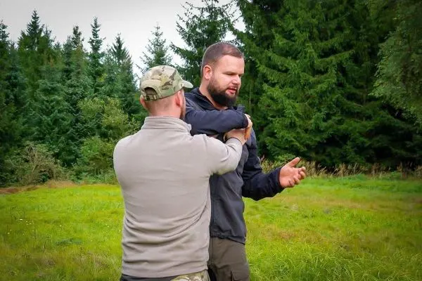 Zwei Personen üben eine Technik zur Kontrolle in einer Wiese mit Bäumen im Hintergrund