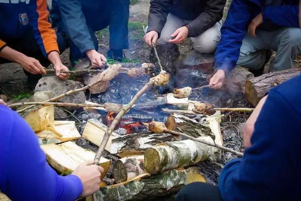 Zweige mit Lebensmitteln über einem offenen Feuer geröstet, Rauch steigt auf