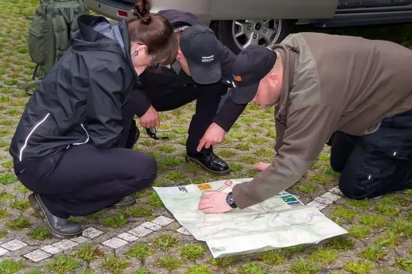 Drei Personen betrachten gemeinsam eine Karte auf dem Boden