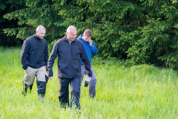 Drei Personen gehen durch hohes Gras in einem Waldgebiet