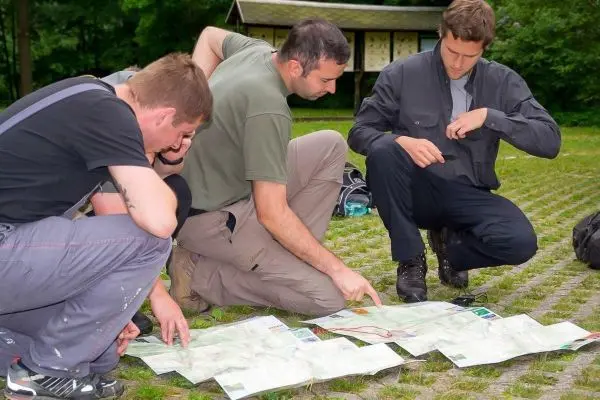 Drei Personen studieren eine ausgebreitete Karte auf dem Boden