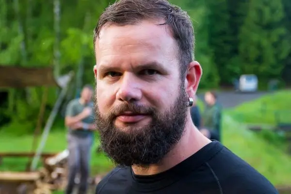 Ein Mann mit Bart trägt ein schwarzes T-Shirt und schaut in die Kamera