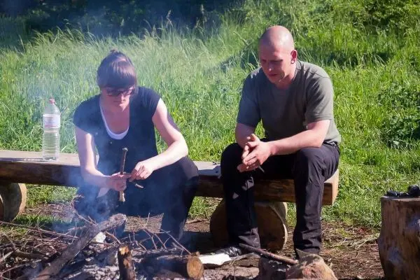 Frau zündet Zunder mit einem Stock über einem kleinen Feuer