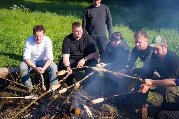 Gruppe von Personen röstet Brot über einem Feuer beim Survival Training