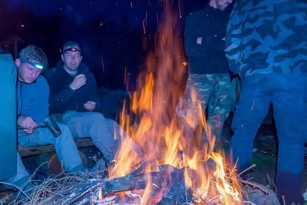 Kleine Flamme brennt in einem Lagerfeuer, umgeben von mehreren Personen