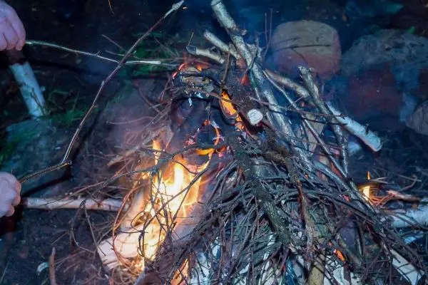 Kleine Flamme lodert zwischen Ästen und Holzstücken