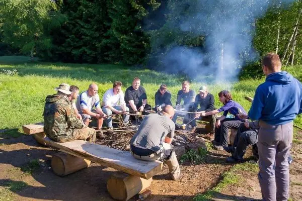 Kleines Bodenfeuer mit Rauch, Gruppe sitzt um Feuerstelle auf Holzbank