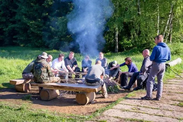 Kleines Bodenfeuer mit Rauch, Teilnehmer sitzen auf Bänken aus Holz