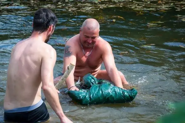 Männer im Wasser heben eine grüne Tasche mit einem Stock