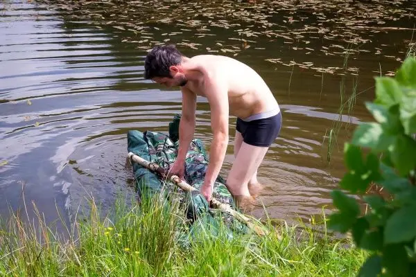 Mann baut improvisierte Trage aus grüner Plane und Holzstöcken im Wasser