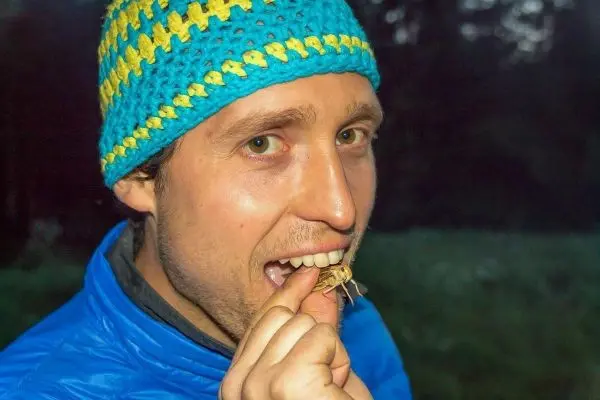 Mann hält einen Käfer zwischen Daumen und Zeigefinger vor den Mund