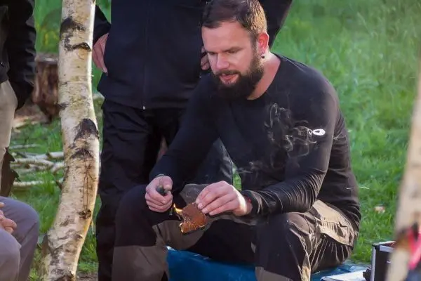 Mann hält rauchendes Holzstück über einer kleinen Flamme
