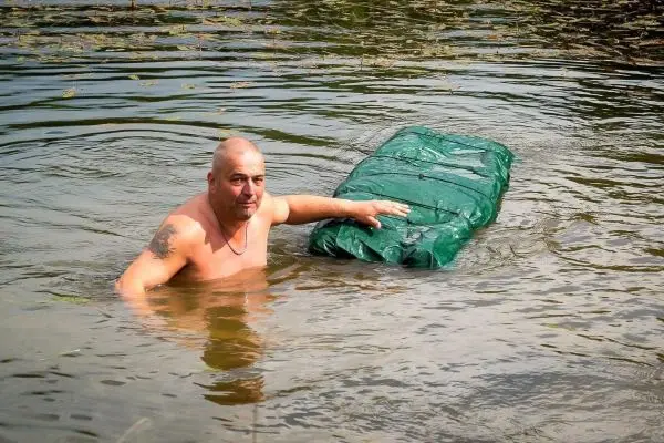 Mann im Wasser stützt sich auf eine grüne, schwimmende Unterlage