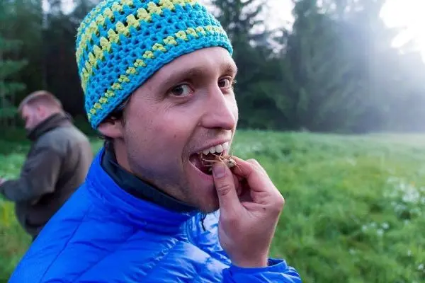 Mann in blauer Jacke isst Insekt im Freien