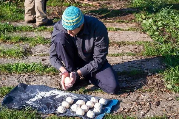 Mann knetet Teig auf einer blauen Plane, daneben liegen mehrere Teigkugeln