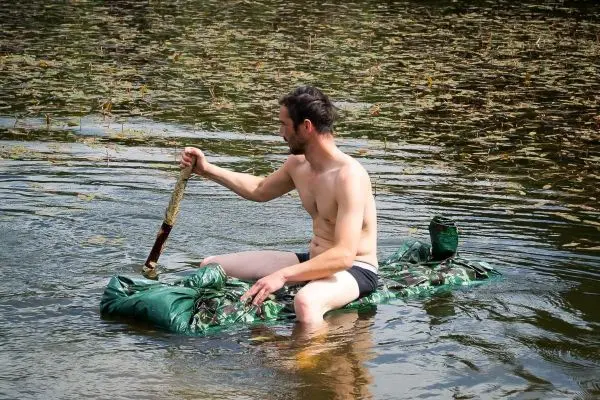 Mann paddelt auf einer improvisierten Schwimmplattform im Wasser