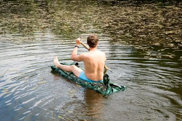 Mann paddelt auf improvisierter Schwimmkonstruktion im Wasser
