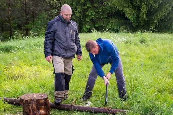 Mann schlägt mit einer Axt auf einen Holzstamm im Gras