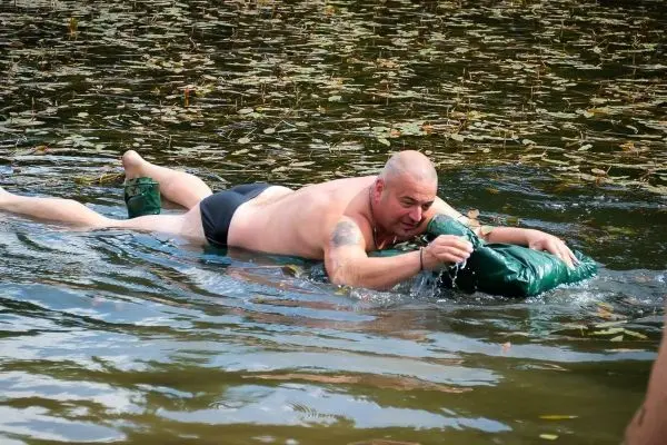 Mann schwimmt auf Wasser mit einer grünen Schwimmhilfe