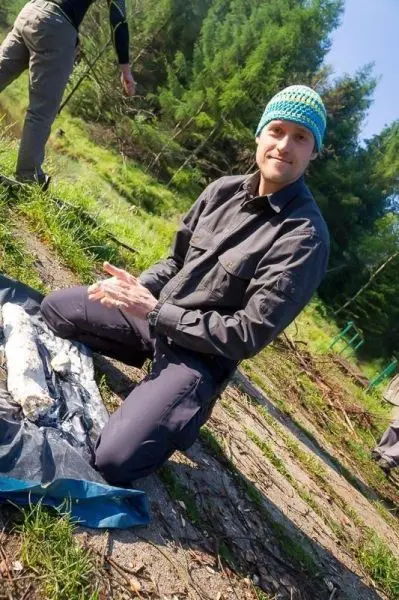 Mann sitzt auf dem Boden und bearbeitet Holzstücke auf einer blauen Plane