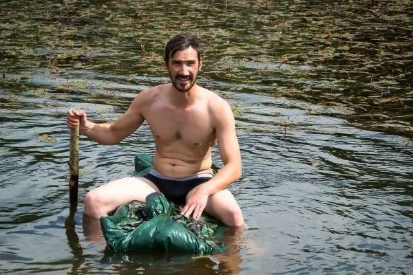Mann sitzt auf einer improvisierten Schwimmhilfe im Wasser und hält einen Stock