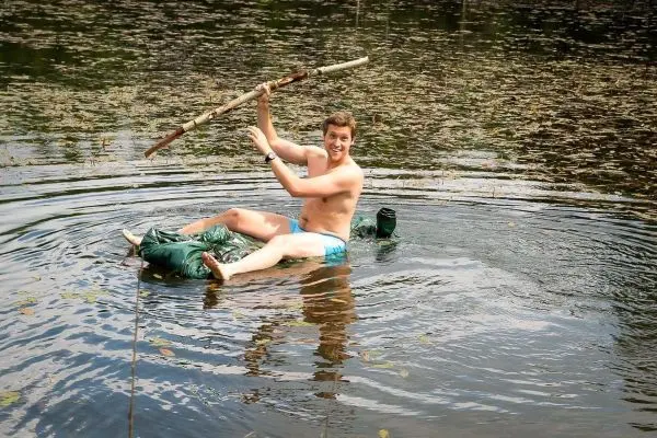 Mann sitzt auf einer improvisierten Schwimmhilfe und hält einen Stock über dem Wasser