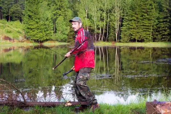 Mann steht am Ufer eines Gewässers mit einer Angelrute in der Hand